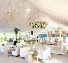 a large white tent with tables and chairs in front of it, surrounded by chandeliers