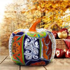 an artistically painted pumpkin sits next to apples