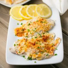 two fish fillets on a white plate with lemon slices and parmesan cheese