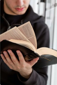 a man is reading a book while wearing a black hoodie and holding it open