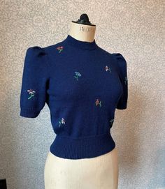 a mannequin wearing a blue sweater with small flowers on the shoulders and sleeves