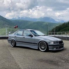 a silver car parked on top of a parking lot next to a mountain covered in clouds