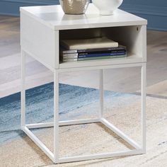 a white end table with a vase and books on it next to a blue rug