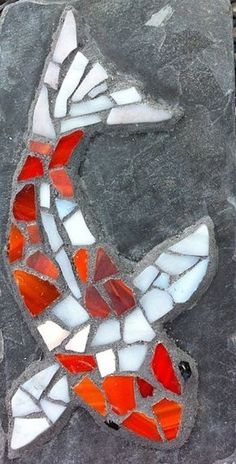 a fish made out of broken glass sitting on top of a gray stone slab with red and white mosaic tiles