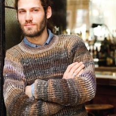 a man with his arms crossed standing in front of a door wearing a knit sweater