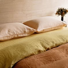 two pillows on top of a bed next to a vase filled with flowers and plants