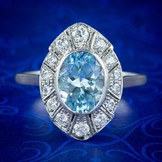 A stunning Art Deco inspired cluster ring built around a gorgeous oval cut aquamarine weighing approx. 1.5ct. It has an icy blue hue and sparkles beautifully in the light along with a frame of bright old European cut diamonds, totalling approx. 0.46ct.  Aquamarine is the birthstone of March. It derives its name from its tranquil, clear blue/ green colouring that emulates the beauty of a tropical ocean or icy glacial waters. It was once believed to be the treasure of Mermaids and is said to bring Light Blue Oval Diamond Topaz Ring, Oval Aquamarine Diamond Ring Fine Jewelry, Oval Aquamarine Diamond Ring In Fine Jewelry Style, Fine Jewelry Light Blue Oval Topaz Ring, Gia Certified Oval Blue Topaz Ring, Light Blue Oval Rings For Anniversary, Blue Topaz Ring With Marquise Cut Center Stone, Blue Marquise Cut Topaz Ring With Center Stone, Gia Certified Oval Aquamarine Jewelry