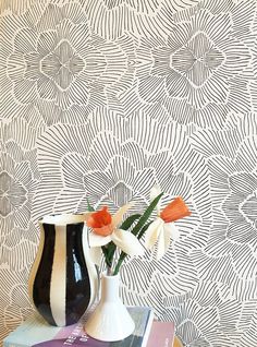 two vases with flowers on top of books in front of a wallpapered background