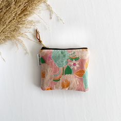 a pink flowered pouch sitting on top of a white table next to dried grass