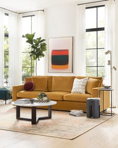 a living room with yellow couches and white curtains on the windowsill, coffee table in front of it