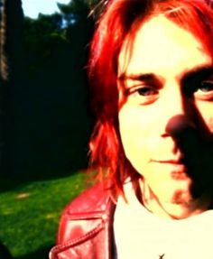 a man with red hair wearing a leather jacket and looking at the camera while standing outside