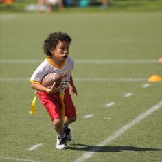 a young boy holding a football on top of a green field with white lines and orange trim