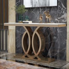 a console table with two statues on it in front of a marble wall and floor