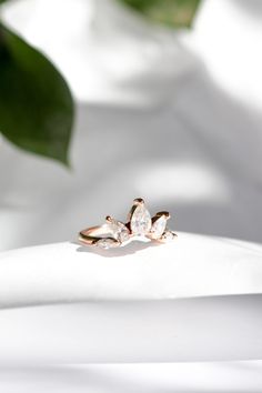 a diamond ring sitting on top of a white cloth next to a leafy plant