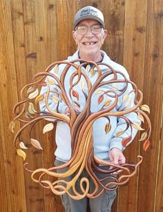 an older man is holding up a tree made out of wood and metal branches with leaves on it