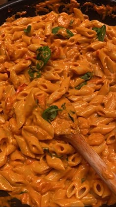 a skillet filled with macaroni and cheese being stirred by a wooden spoon