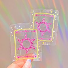 two stickers with the sun and stars on them are being held in front of a holographic background