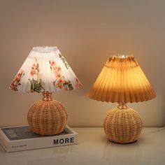 two wicker lamps sitting next to each other on a table with a book and lamp shade