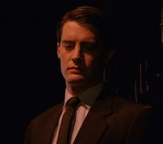 a man wearing a suit and tie in the dark with his eyes closed, staring at something