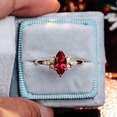 a person holding a ring with a red stone in it's center and diamond accents around the band