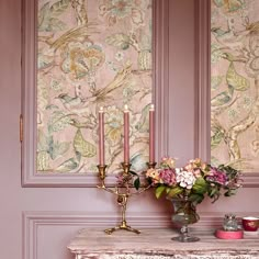 a vase with flowers and candles on a table in front of a wallpapered background