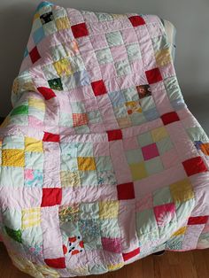 a pink and yellow patchwork quilt sitting on top of a wooden floor next to a white wall