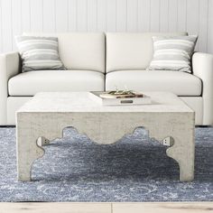 a white couch sitting next to a table on top of a blue rug in a living room