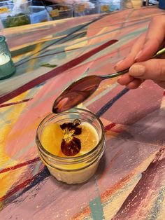 a person holding a spoon over a jar filled with food on top of a table