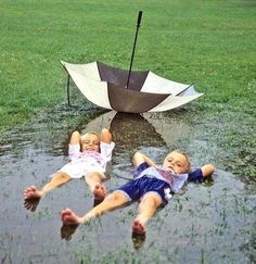 two children are laying in the water with an umbrella over them and one is upside down