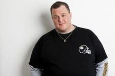 a man standing in front of a white wall wearing a black shirt with a football helmet on it