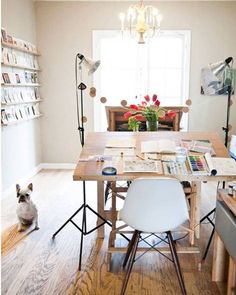 a dog sitting on the floor in front of a dining room table with chairs and bookshelves