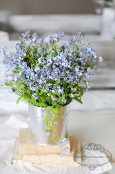 blue flowers are in a silver vase on a table