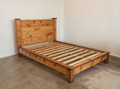 a bed frame made out of wood in a room with concrete flooring and white walls