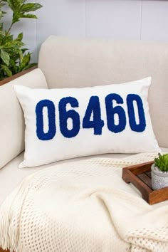 a white couch with a blue and white pillow on top of it next to a potted plant