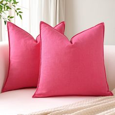 two pink pillows sitting on top of a white couch next to a potted plant