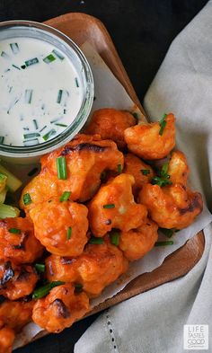 a wooden tray topped with fried food next to a small bowl of ranch dressing and cucumber