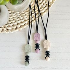 three necklaces with different colored beads and black cords on a white table next to a potted plant