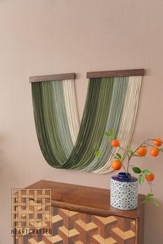 a vase with oranges on top of a wooden table next to a wall hanging