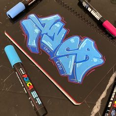 a notebook with blue graffiti on it next to crayons and markers