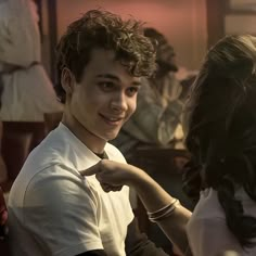 a young man smiles as he sits next to a woman in a white shirt and black pants