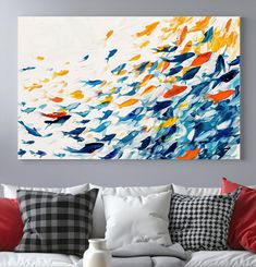 an abstract painting hangs on the wall above a white couch with red and blue pillows