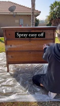 a woman sitting on the ground next to a chest of drawers that says spray easy off