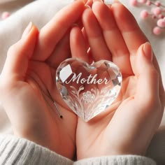 a person holding a crystal heart in their hands with the word mother written on it