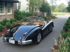 an old fashioned sports car is parked on the side of the road in front of a house