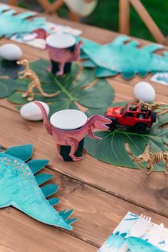 dinosaur paper plates and cups on a wooden table with green leaves, dinosaurs and cars in the background