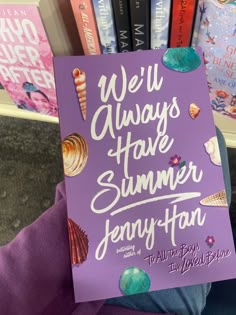 a person holding up a purple book in front of bookshelves with pink covers