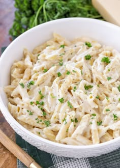 a white bowl filled with pasta and parsley on top of a wooden cutting board