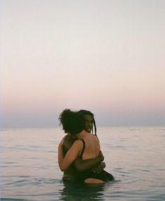 two people are hugging in the water at sunset or dawn, one is sitting on his back