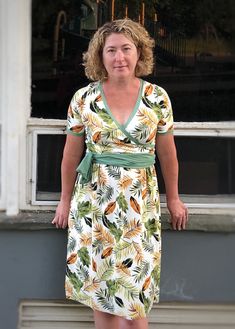 a woman standing in front of a window with her hands on her hips wearing a dress