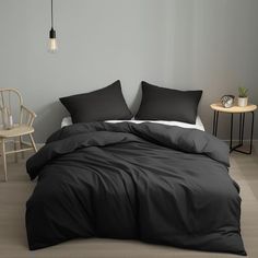 a bed with black comforter and pillows in a room next to a white chair